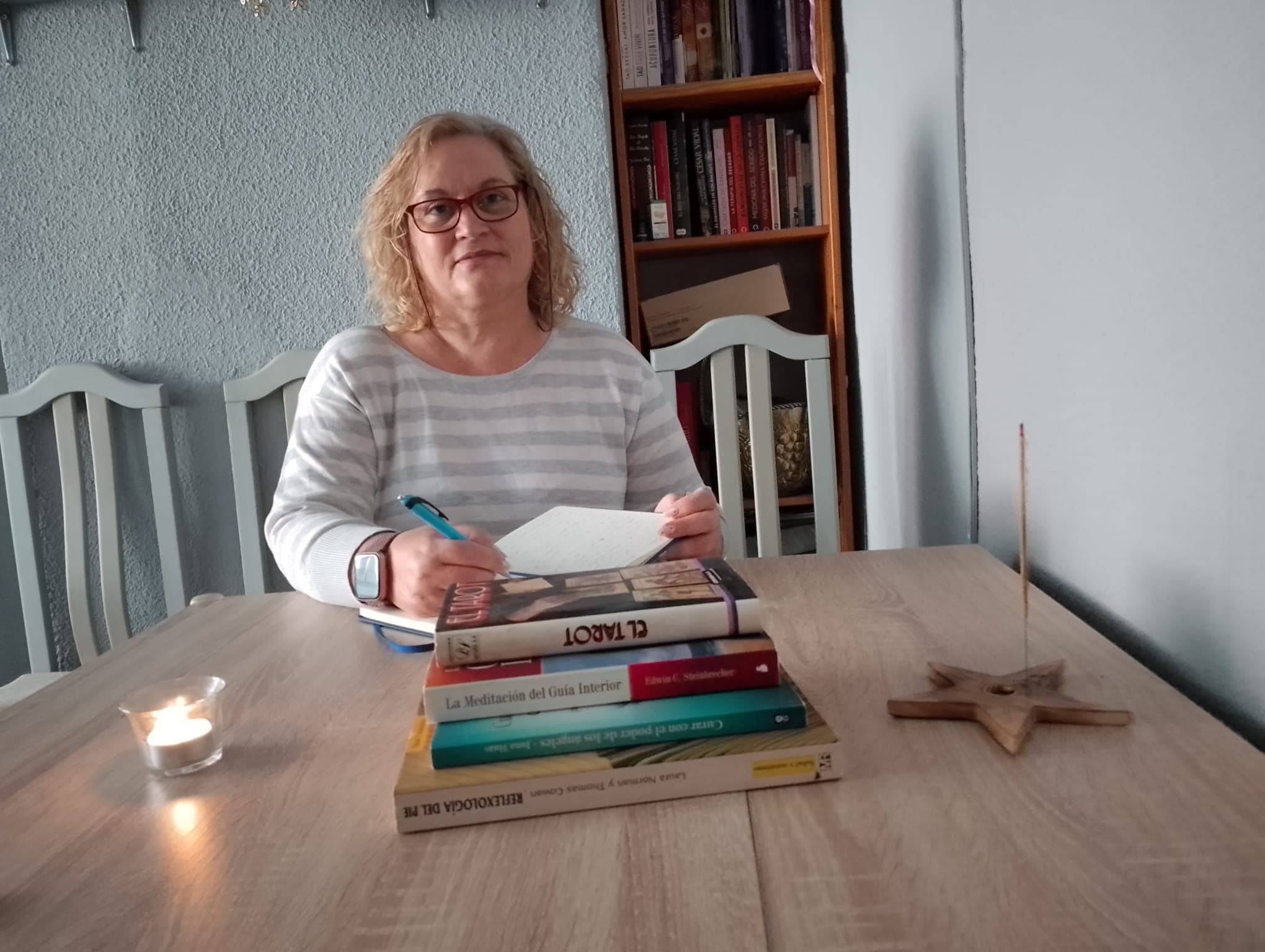 Teresa Ovejero escribiendo en su consulta, rodeada de libros de reflexología, tarot y meditación